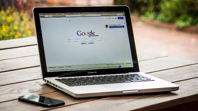 Image of a laptop on a table displaying Google's homepage.